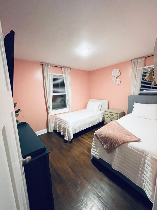 Un dormitorio con dos camas, una mesita de noche, un tocador y una ventana con cortinas.