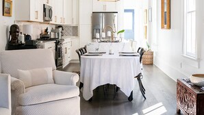 Una cocina amplia con armarios blancos, un comedor con mesa blanca y una lámpara colgante moderna.