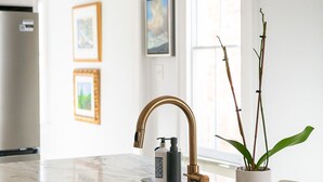 Una cocina con encimera de mármol, grifo dorado y planta en maceta.