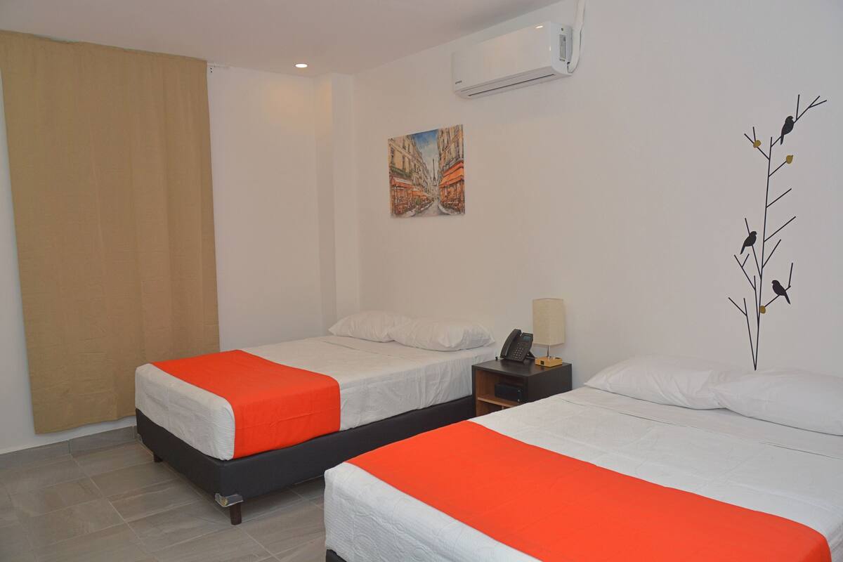 Une chambre d’hôtel avec deux lits, chacun recouvert d’une couverture orange, agrémenté d’oreillers blancs et doté d’une petite table de chevet avec une lampe.