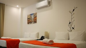 Ein Hotelzimmer mit zwei Betten, jeweils mit weißer Bettwäsche und roten Tagesdecken. An der Wand hängt ein Gemälde, ein Telefon und eine Wandklimaanlage.