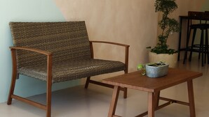 Ein Zimmer mit einem Korbstuhl, einem Holztisch und einer Topfpflanze.