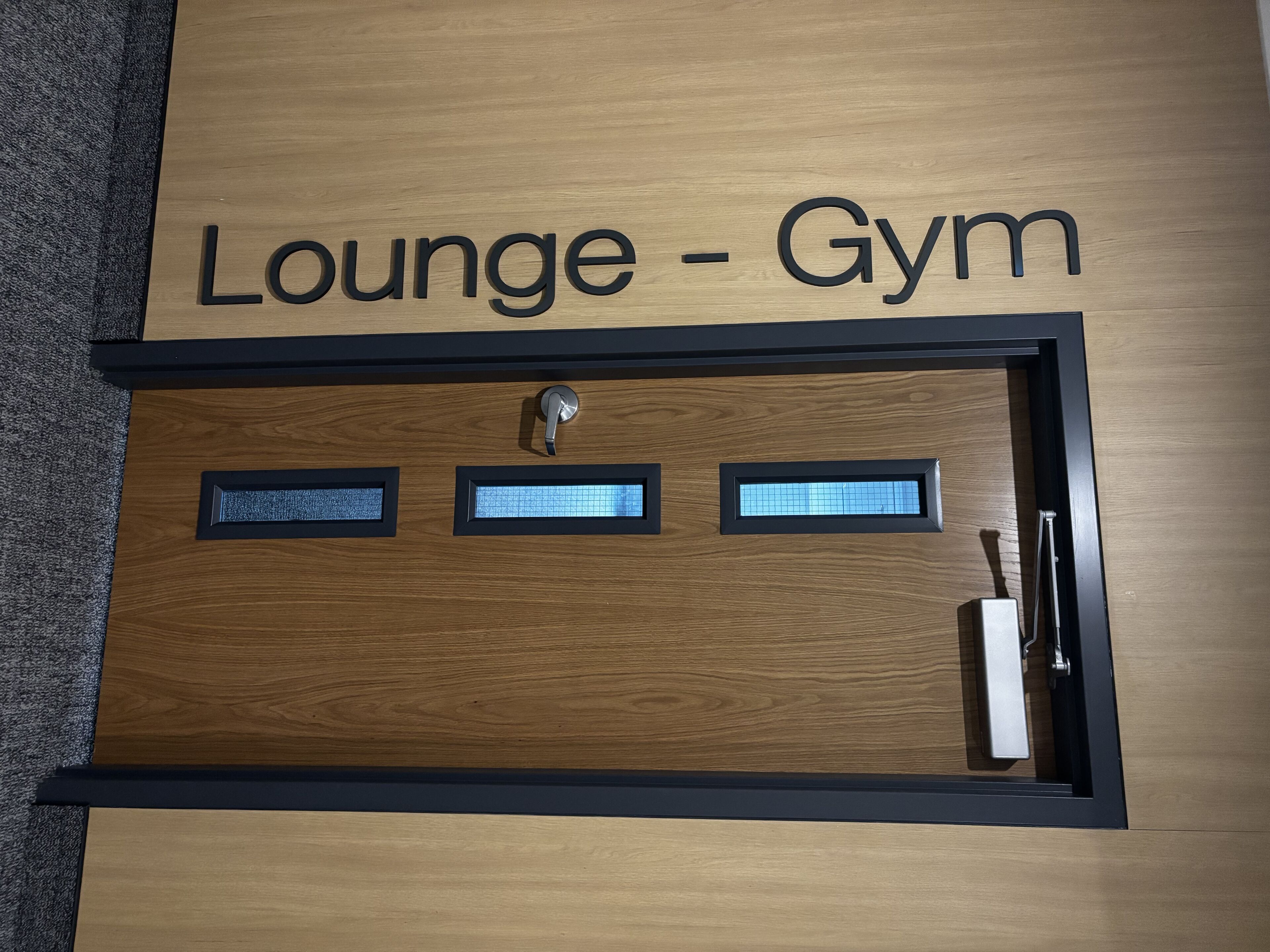 Una puerta de madera con la inscripción 'Lounge - Gym' en la parte superior, que indica un espacio multifuncional.