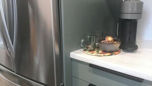 Ein Edelstahl-Kühlschrank, eine Kaffeemaschine und eine Schüssel mit Dekorationen auf einer Küchenarbeitsplatte.