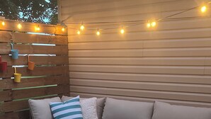 Ein gemütlicher Außenbereich mit einer gepolsterten Couch, einem Glastisch und Lichterketten.