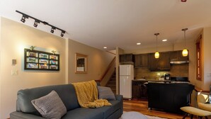 Un salon moderne avec un canapé, un pouf et une cuisine en arrière-plan.