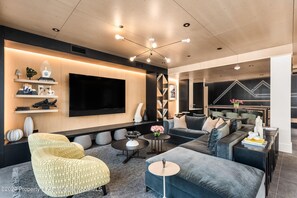 Un soggiorno moderno con un'ampia televisione a schermo piatto, posti a sedere confortevoli e una parete decorativa con un motivo luminoso geometrico.