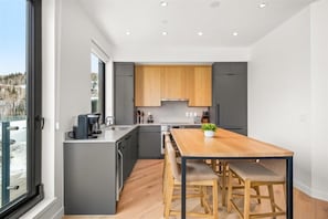 Una cucina moderna con mobili grigi, un tavolo da pranzo in legno e vista su un paesaggio innevato attraverso un'ampia finestra.