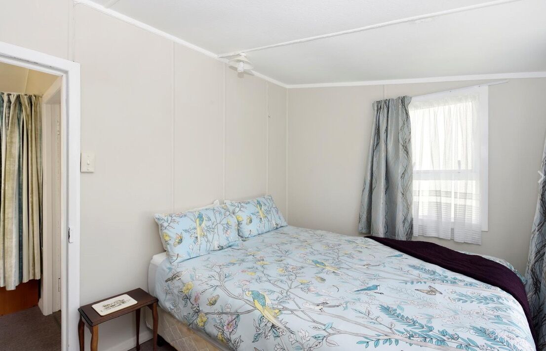 A bedroom with a bed, a nightstand, a window with curtains, and a door with curtains.
