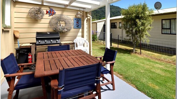 An outdoor patio with a grill, chairs, and a table. - Okiwi Bay Cosy Cottage (Ōkiwi Bay)