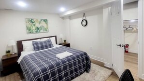 A bedroom with a bed, a nightstand, a wall clock, and a door leading to another room. - New Private Spacious & Modern Apartment near Square One and Downtown Mississauga (Mississauga)
