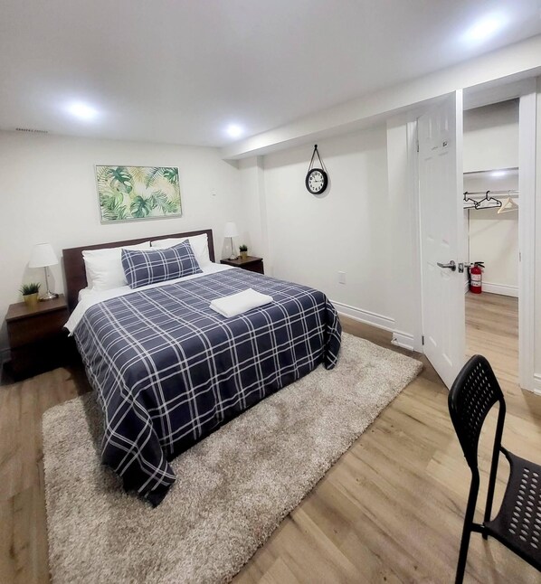 A bedroom with a bed, a nightstand, a wall clock, and a door leading to another room.