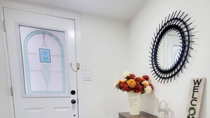 A white door with a frosted glass panel and a sign indicating a lock and lights. A wooden console table with a vase of flowers and a 'WELCOME' sign is against the wall. - New Private Spacious & Modern Apartment near Square One and Downtown Mississauga (Mississauga)