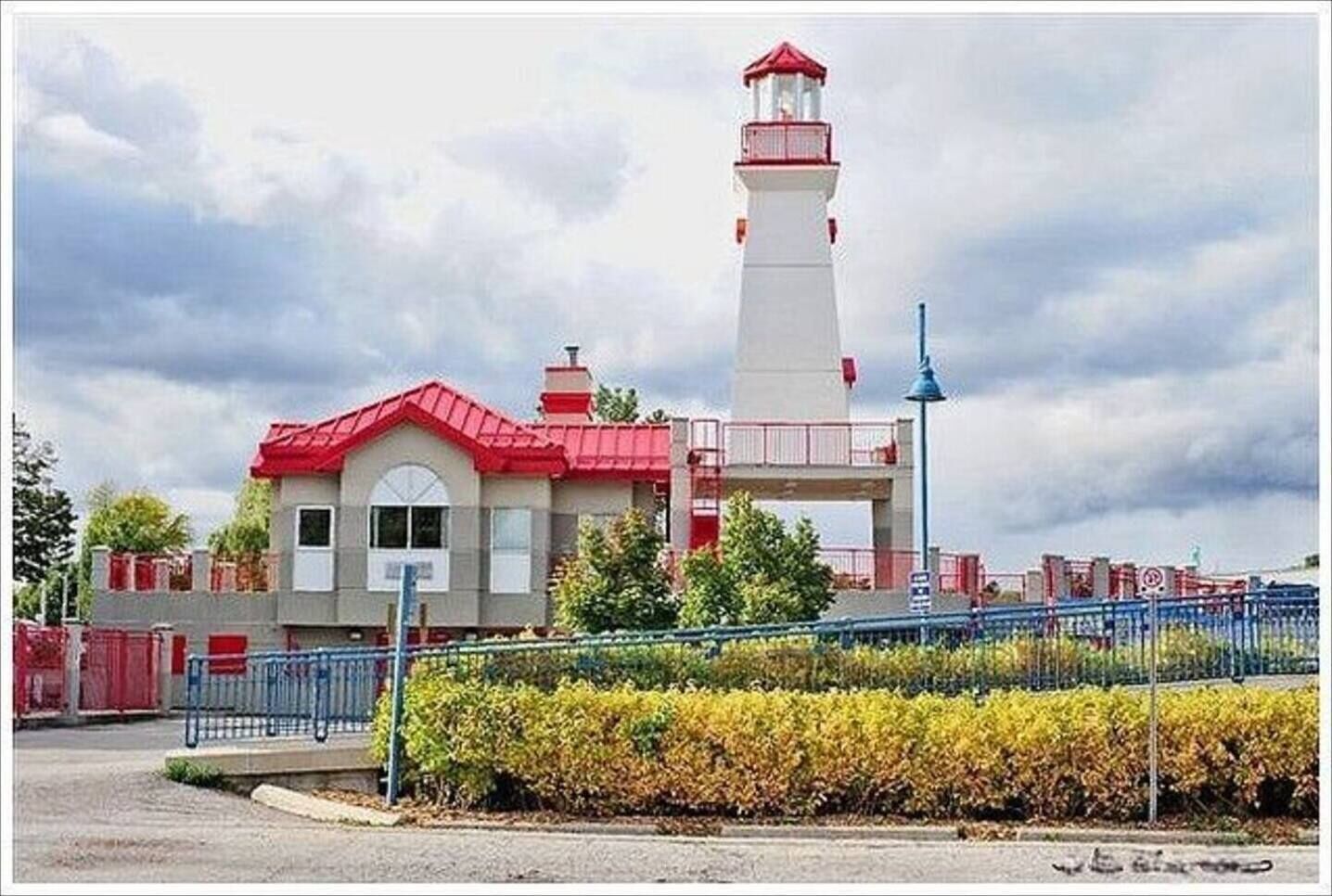 Un faro con techo rojo y torre blanca, rodeado de una valla y arbustos.