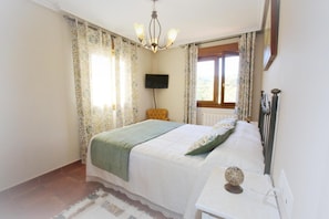 Ein Schlafzimmer mit Bett, Fernseher, Fenster und Stuhl.