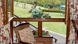 A wicker chair with a cushion, a window with curtains, and a view of a garden. - Holiday Home 'Supereda' with Mountain View, Private Terrace and Wi-Fi (San Juan de Parres)