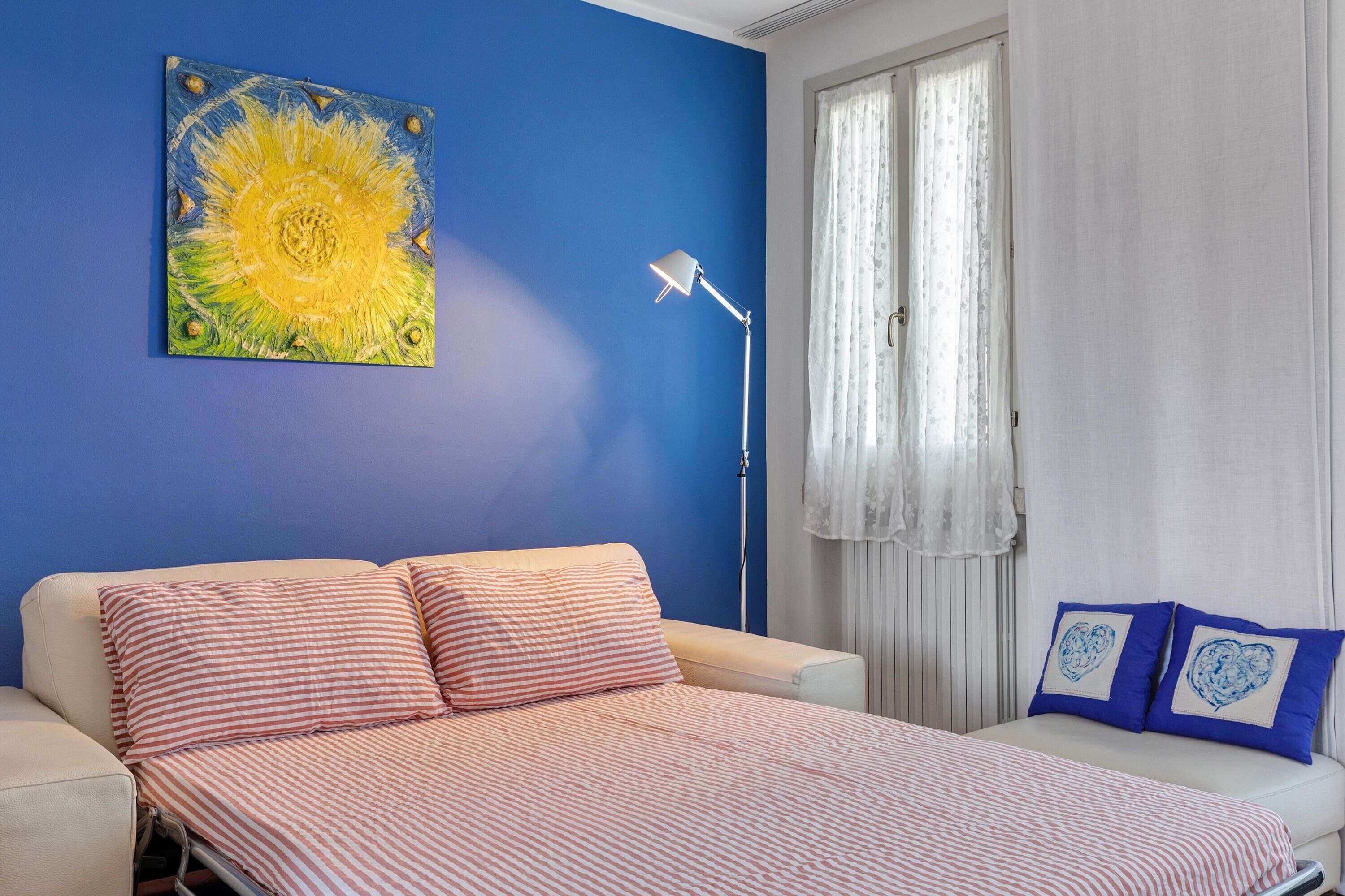 A room with a bed, a lamp, a painting, and a window with curtains.