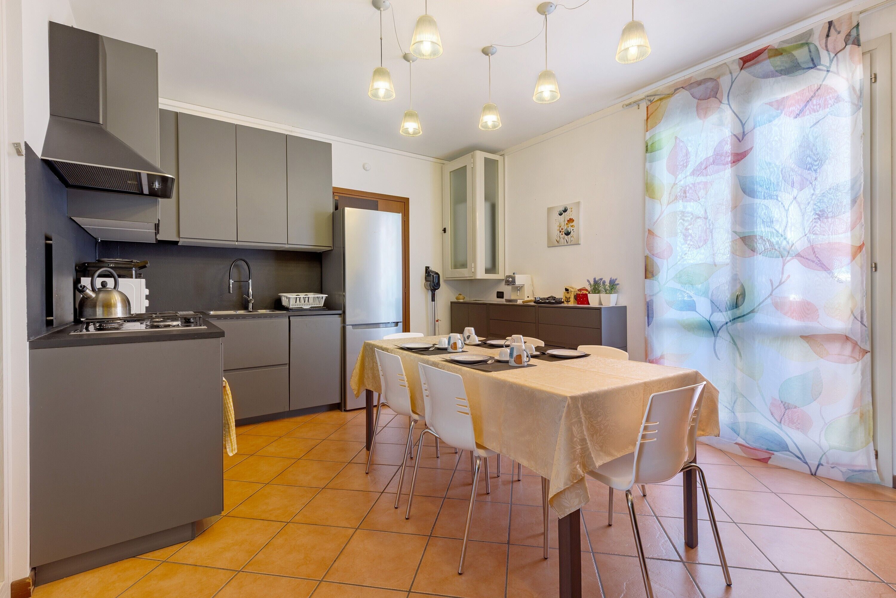 A kitchen with grey cabinets, a dining table with chairs, and a tiled floor.