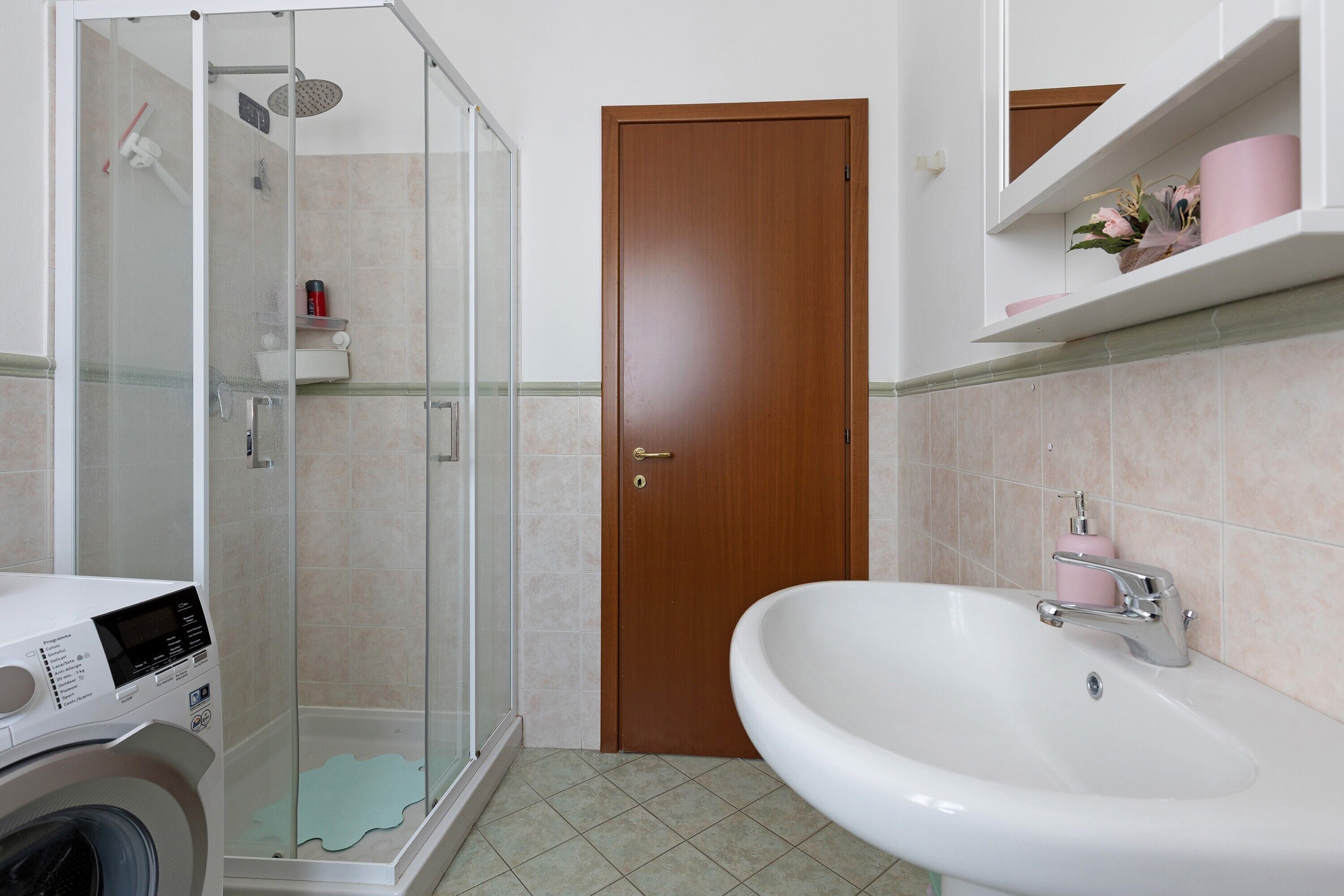Ein Badezimmer mit Duschkabine, Holztür, Waschbecken und Waschmaschine.