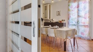 Comedor con mesa dispuesta para cuatro, cocina al fondo y una cortina con estampado de hojas coloridas.
