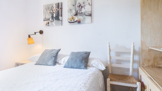A neatly made bed with pillows, a bedside lamp, and two wall-mounted paintings.