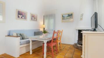 Un comedor con una mesa de vidrio, sillas de madera, un sofá blanco y un televisor.