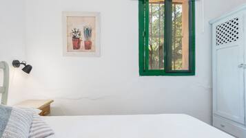 Une chambre à coucher comprenant un lit, une table de chevet, une lampe, une fenêtre avec des volets verts, un tableau accroché au mur et une armoire.