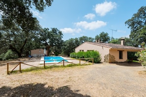 A house with a swimming pool, surrounded by trees and a gravel driveway.