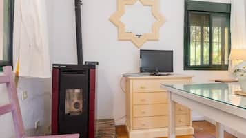 A room with a wood-burning stove, a TV on a dresser, a glass table, and a window with a view of trees.