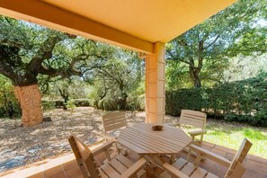 An outdoor patio with a table and chairs, surrounded by trees and greenery.