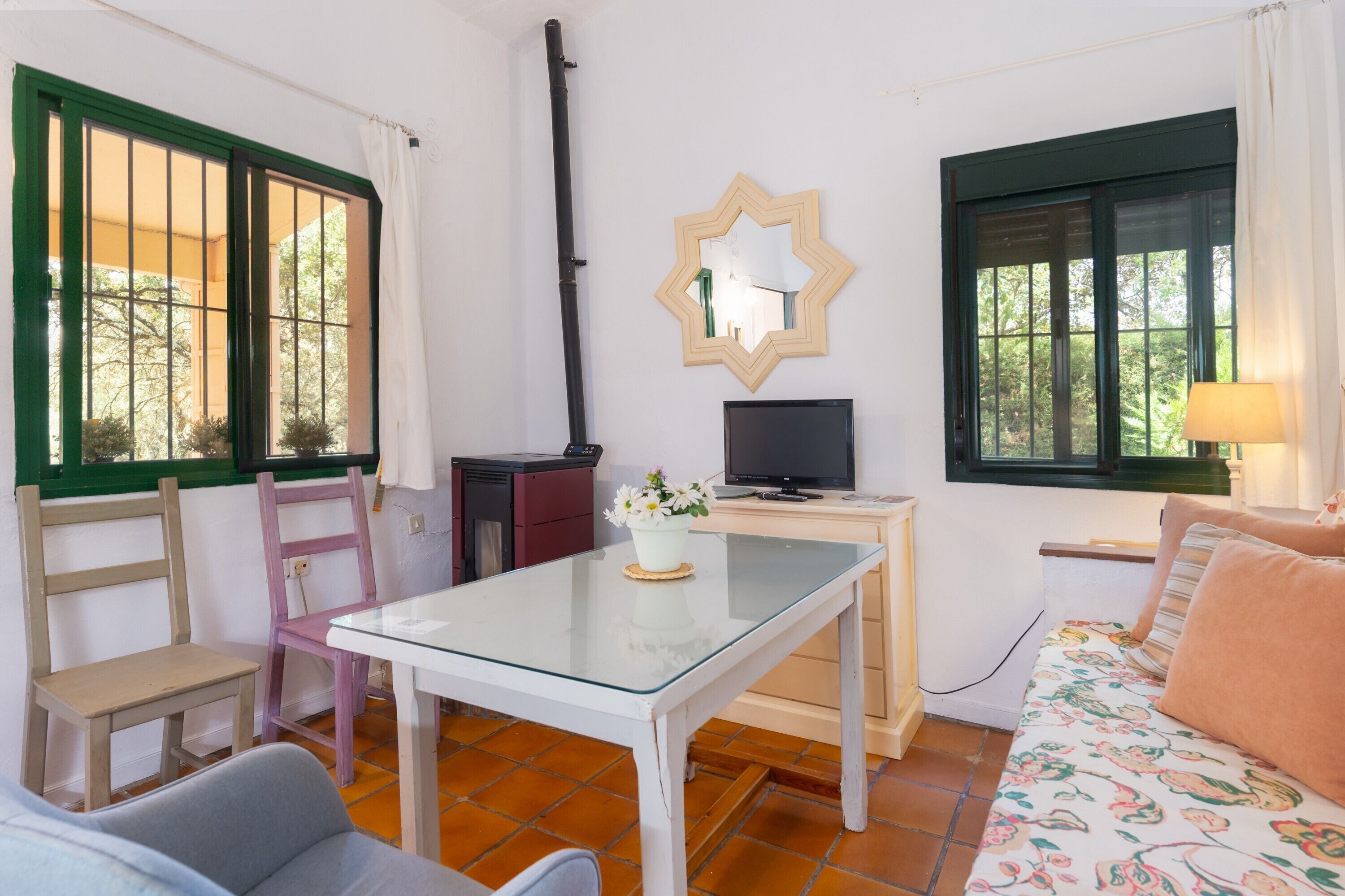 Quarto com mesa de vidro, televisão, cadeira, sofá e janela com cortina.