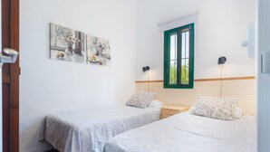 A room with two beds, a window with green shutters, wall art, and a bedside lamp. - Rural House El Chopo with Mountain Views, Terrace, Shared Pool, and Parking (Alajar)