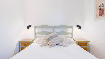 Una cama con cabecera, dos mesitas de noche y una lámpara fijada a la pared.