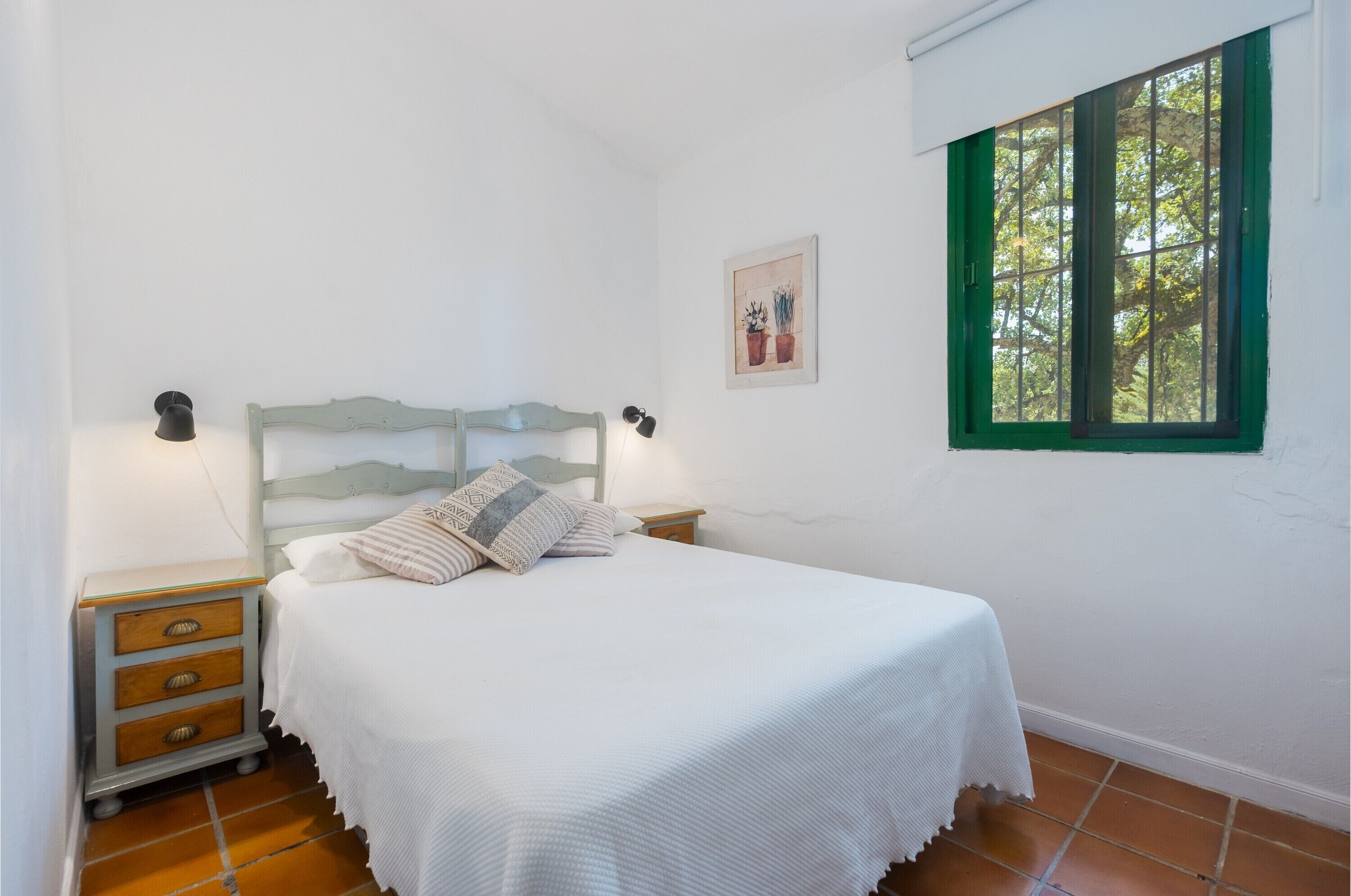 Een slaapkamer met een bed, nachtkastjes, een raam en een aan de muur bevestigd schilderij.