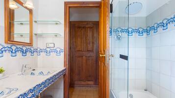 A bathroom with a wooden door, a glass shower enclosure, and a white sink with blue patterned tiles.
