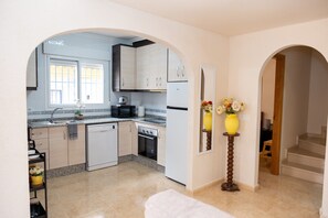 A kitchen with a dishwasher, oven, and microwave. There are two archways leading to other rooms.