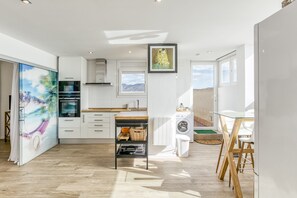 Une cuisine moderne avec des meubles blancs, un four encastré et une fenêtre donnant sur un paysage montagneux.
