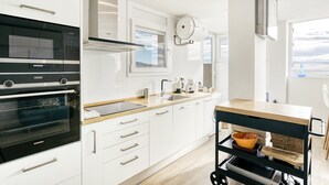 Una cocina moderna con armarios blancos, horno empotrado, microondas y un amplio ventanal.