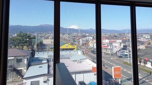 A view through a window with a mesh screen, displaying a cityscape with buildings, a mountain, and a clear sky. - HOTEL KUNIMI KAMONOMIYA (Odawara)
