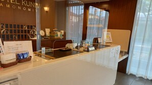 A hotel reception area with a counter, a sign reading "Hotel Kunin Amonomi," and a window with a view of the outside. - HOTEL KUNIMI KAMONOMIYA (Odawara)