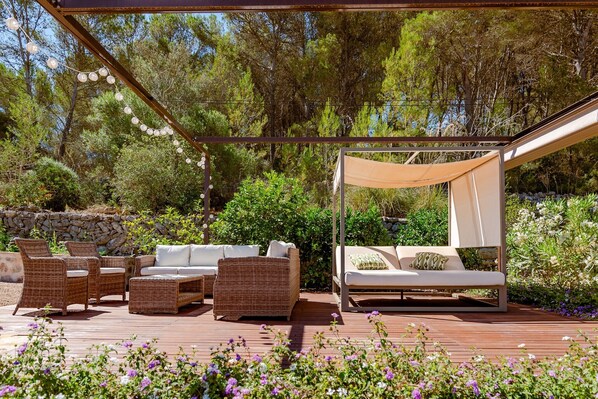 An outdoor patio with wicker furniture, a canopy, and a stone wall backdrop.