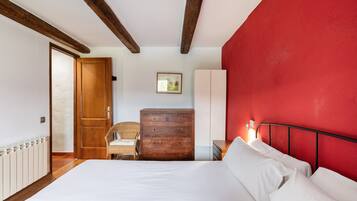 Ein Schlafzimmer mit Bett, Holzkommode, Stuhl und einer roten Akzentwand.