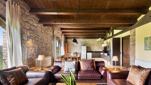 A living room with leather sofas, a coffee table with a plant, stone walls, wooden beams, and a kitchen in the background. - Country House 'Casamira' with Mountain View, Private Pool and Wi-Fi (Unknown)