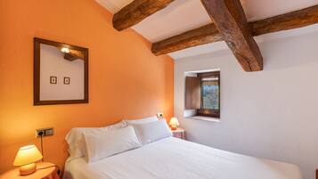 Un dormitorio con cama, lámparas de noche, ventana y vigas de madera a la vista.