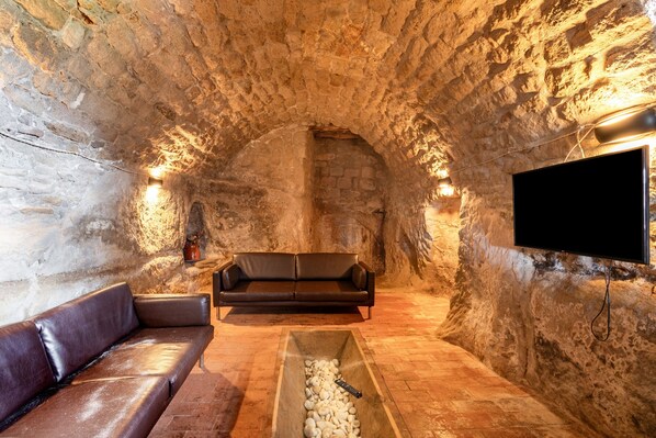 A stone-walled room with a leather sofa, a television, and a stone basin.