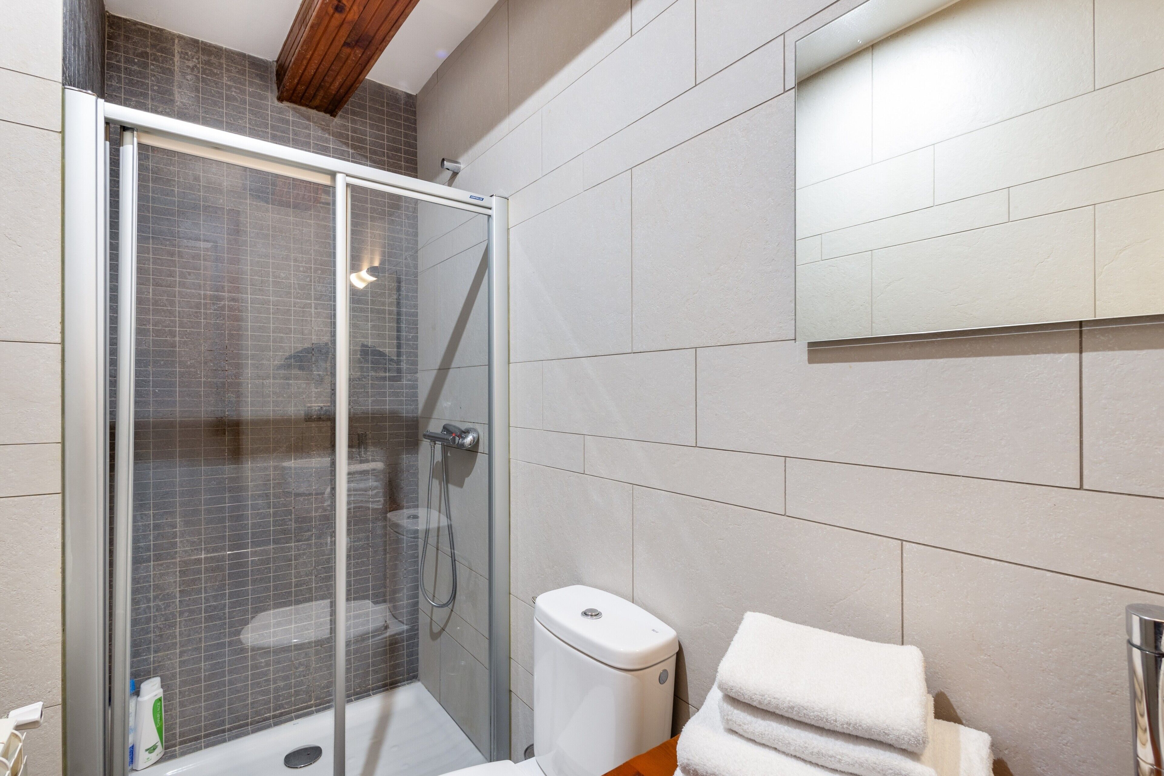 Une salle de bain moderne avec une douche à parois de verre, des toilettes et une pile de serviettes blanches.