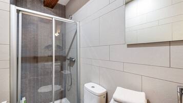 Une salle de bain moderne avec une douche à parois de verre, des toilettes et une pile de serviettes blanches.