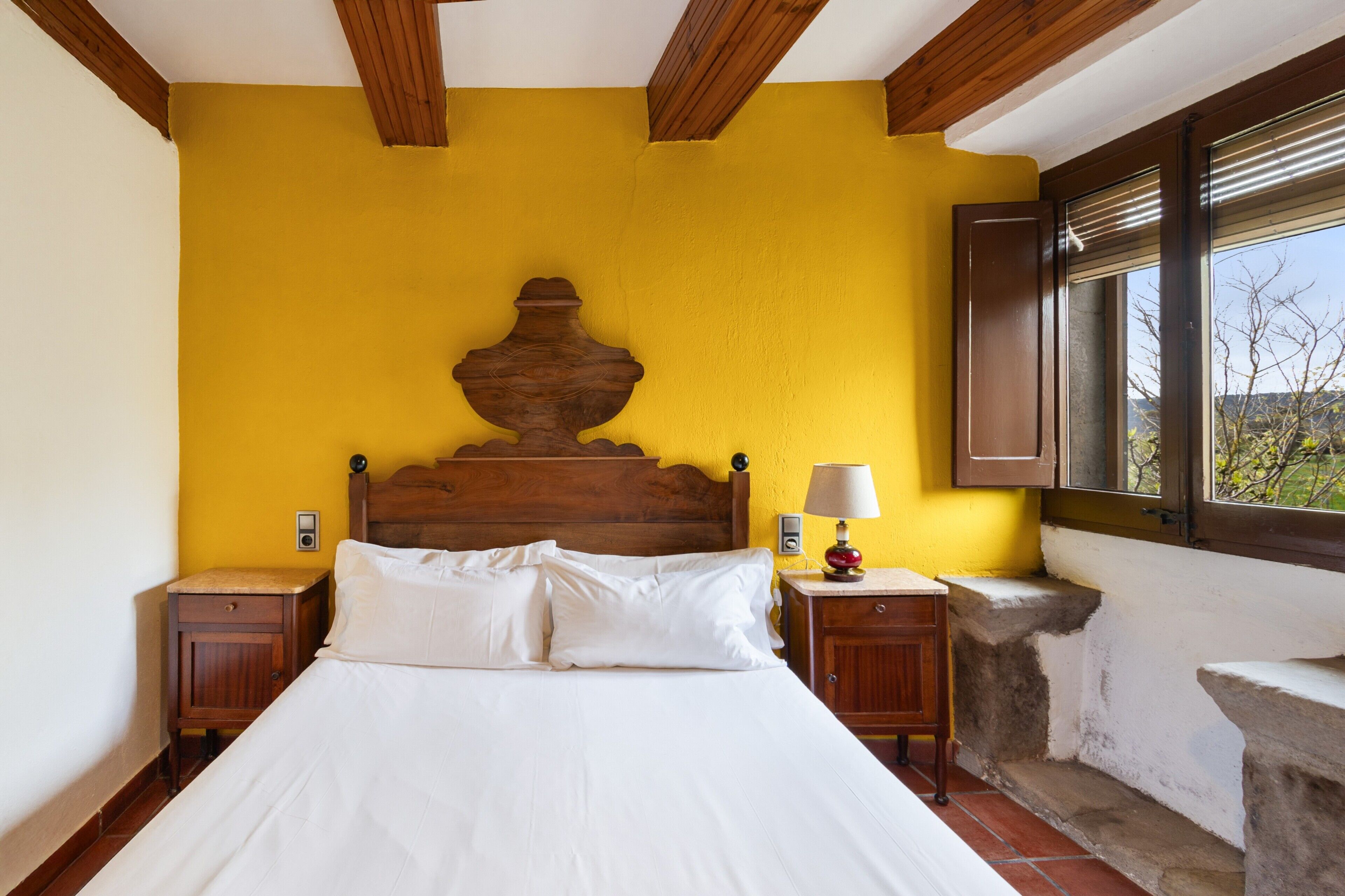 Una camera da letto con testiera in legno, un letto con lenzuola bianche, un comodino, una lampada da letto e una finestra con vista.
