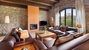 A furnished living room with stone walls, a fireplace, a television, and a large window with curtains. - Country House 'Casamira' with Mountain View, Private Pool and Wi-Fi (Unknown)