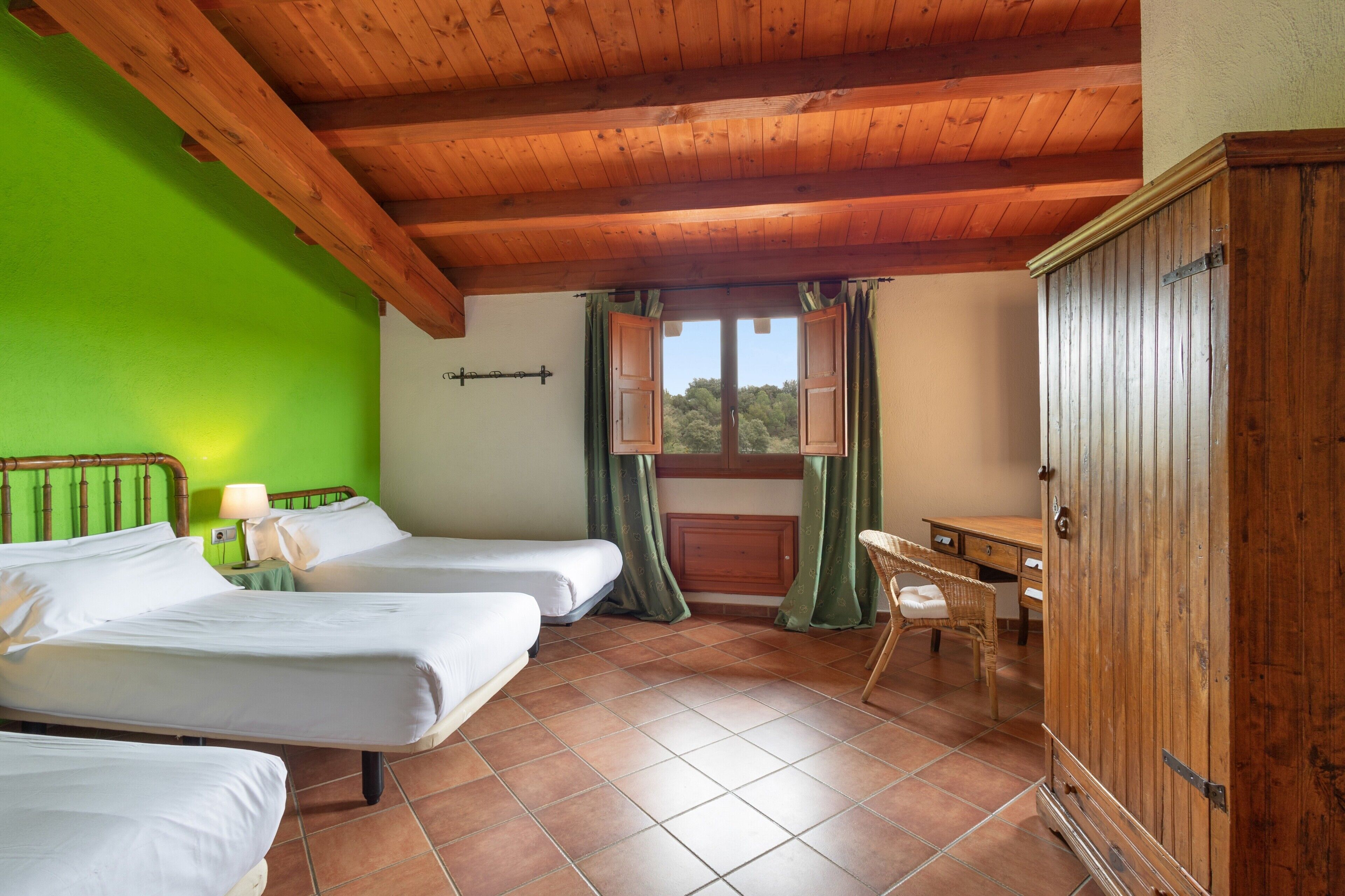 A room with two beds, a wooden wardrobe, a desk, and a window with curtains.